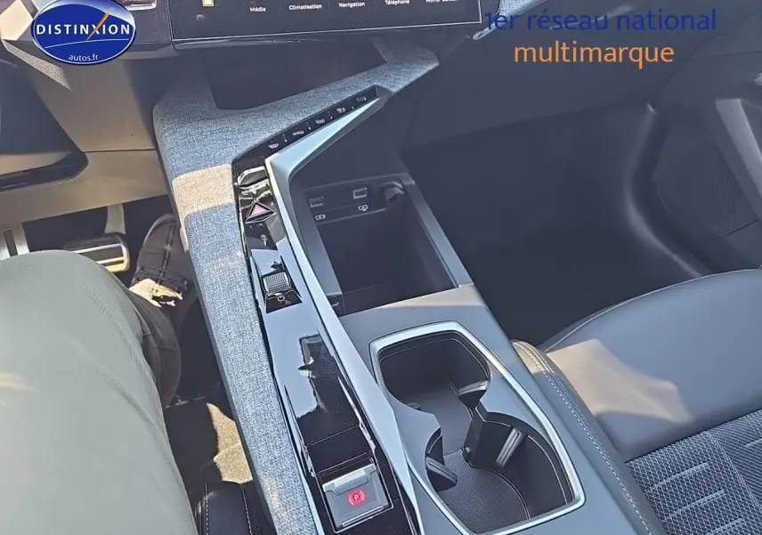 Vue intérieure centrée sur la console centrale et accoudoir du Peugeot 5008 Hybrid 145 gris titane, avec sellerie cuir et tissu.