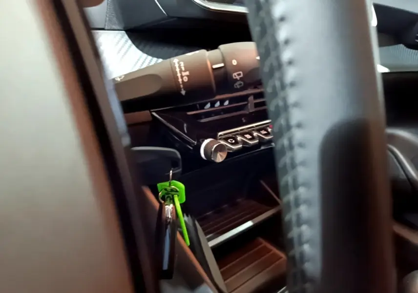 Détail intérieur du tableau de bord et commandes de la Peugeot 208 blanc, avec clé verte suspendue près du volant.