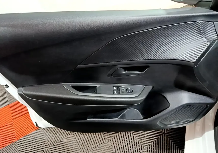 Vue intérieure du panneau de porte avant gauche de la Peugeot 208 blanche, avec commandes de vitres et insert effet carbone.
