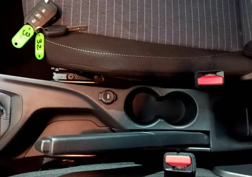 Vue rapprochée de la console centrale intérieure avec frein à main, porte-gobelets et clé de Peugeot 208 blanche.