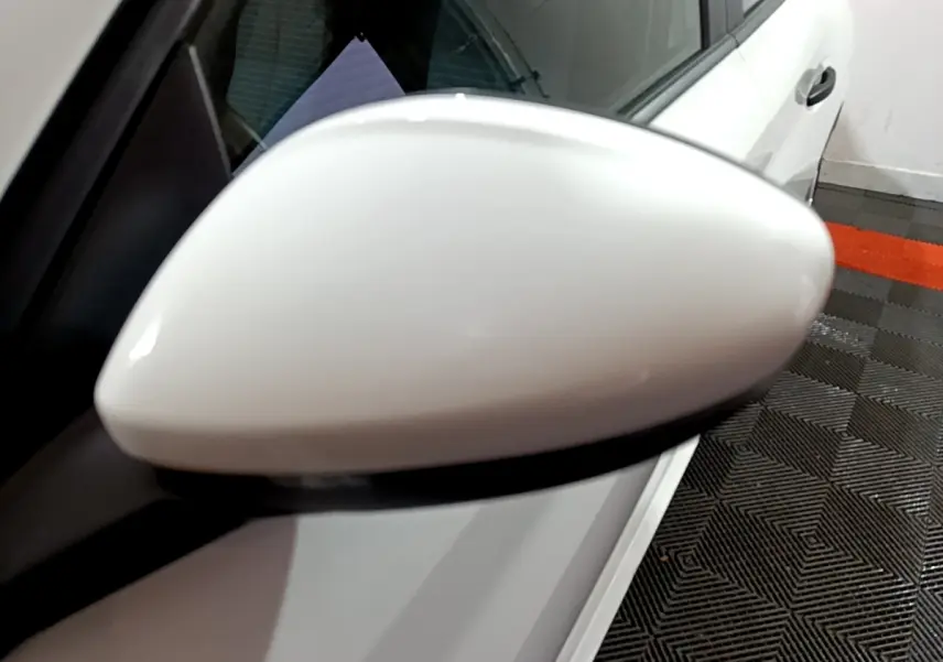 Rétroviseur côté gauche blanc d'une Peugeot 208 1.5 BlueHDi 100 S&S Premium vue en gros plan, avec portière blanche visible.