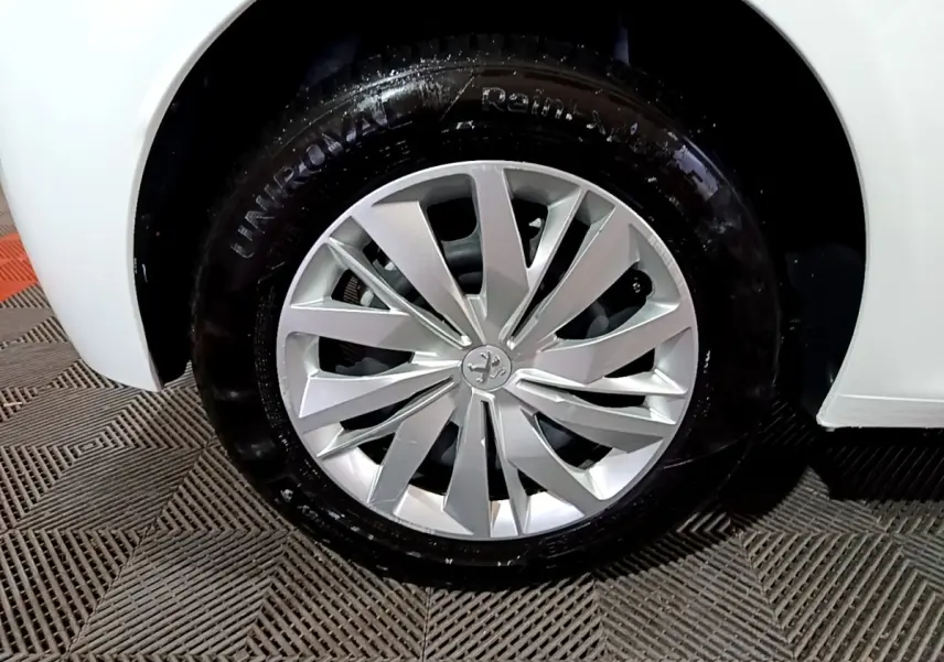 Gros plan sur la roue avant droite d’une Peugeot 208 blanche, mettant en valeur la jante alliage au design moderne.
