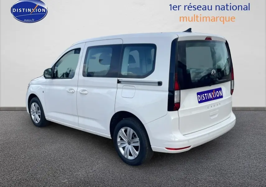 Vue 3/4 arrière droite d'un Volkswagen Caddy blanc 2025 avec vitres teintées et barres de toit visibles.