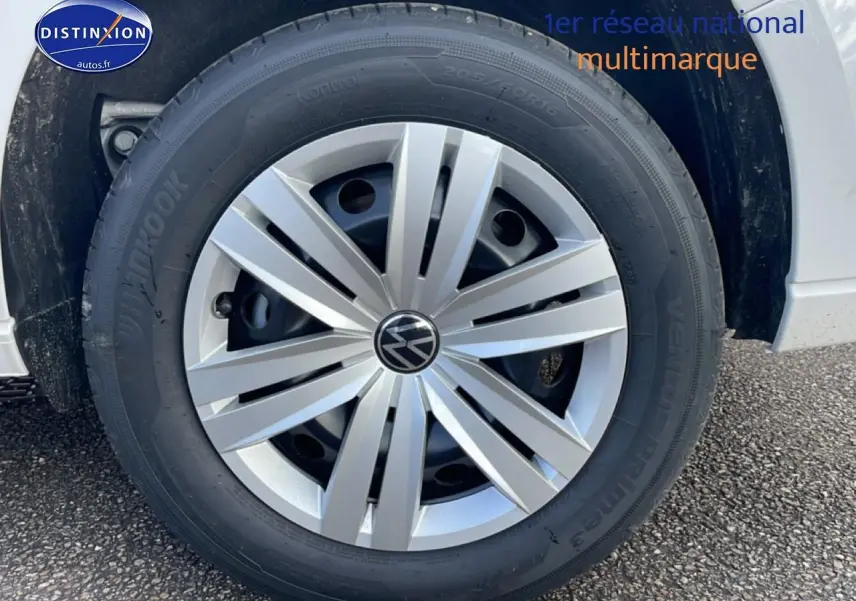 Gros plan sur la roue avant droite d’un Volkswagen Caddy blanc avec jante argentée et logo VW central.