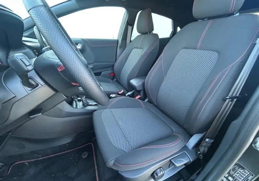 Vue intérieure côté conducteur du Ford Puma gris Magnetic 2023, sièges noirs avec surpiqûres rouges et volant perforé.