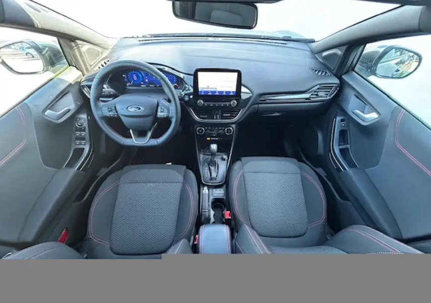 Vue intérieure avant du Ford Puma gris Magnetic 2023, volant ST-Line à méplat avec surpiqûres rouges et écran tactile central.