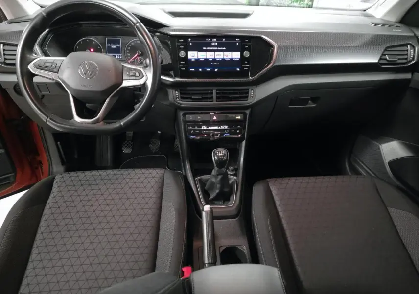 Vue intérieure frontale du tableau de bord et volant cuir noir du Volkswagen T-Cross 1.0 TSI 110 Active, avec levier de vitesses manuel.