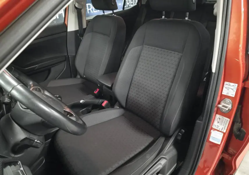 Vue intérieure côté conducteur du Volkswagen T-Cross orange, mettant en valeur les sièges avant en tissu noir avec motifs géométriques.