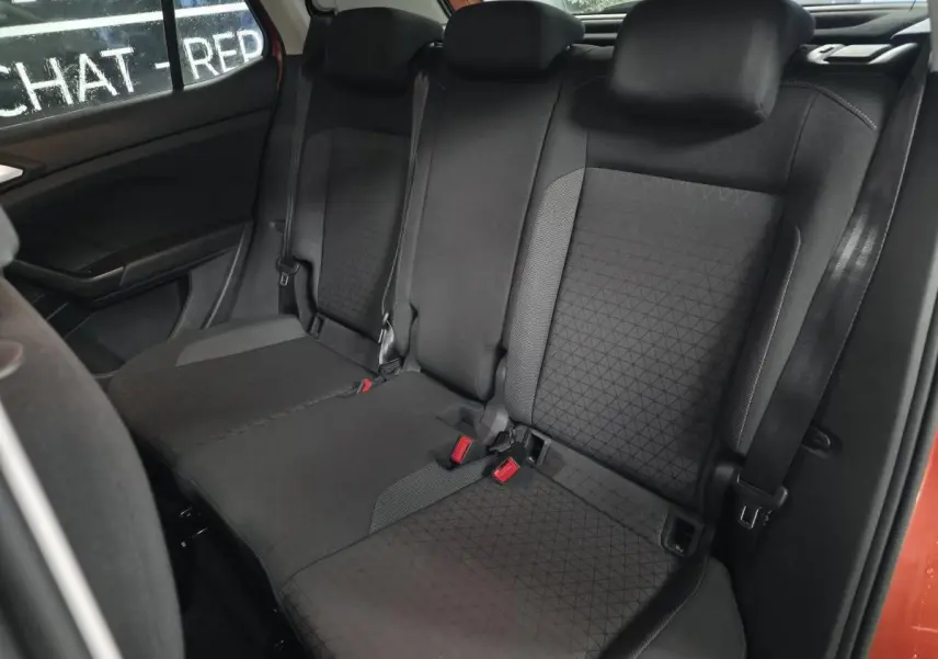 Vue intérieure montrant la banquette arrière noire du Volkswagen T-Cross orange, avec appuis-tête et ceintures visibles.