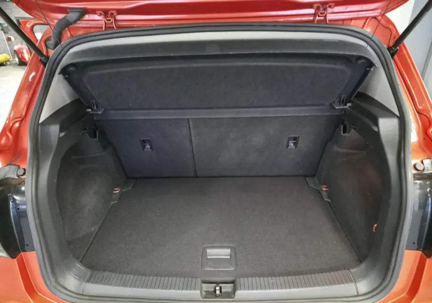 Coffre ouvert d'un Volkswagen T-Cross orange, vue arrière montrant l'espace de chargement vide et la tablette cache-bagages.