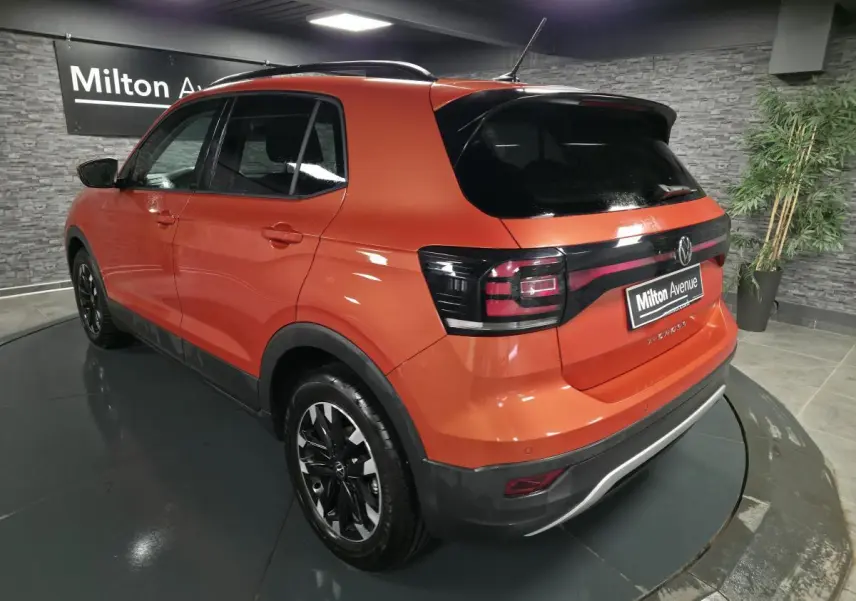 Vue 3/4 arrière gauche d'un Volkswagen T-Cross orange Energy avec vitres arrière surteintées et jantes alliage noires.