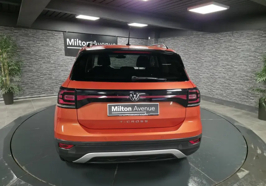 Vue arrière d'un Volkswagen T-Cross orange métallisé avec feux arrière noirs et logo VW central.