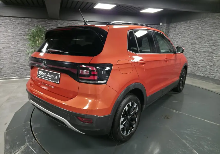 Vue 3/4 arrière droite d'un Volkswagen T-Cross orange métallisé avec vitres arrière surteintées et jantes alliage noires.