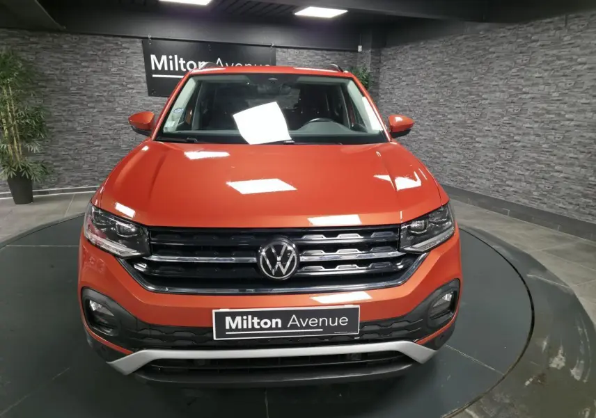 Vue avant d'un Volkswagen T-Cross orange métallisé avec calandre noire et détails chromés, en showroom.