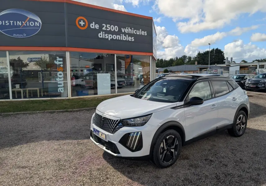 Peugeot 2008 blanc vue 3/4 avant droit avec toit noir et jantes alliage bi-ton devant un concessionnaire.