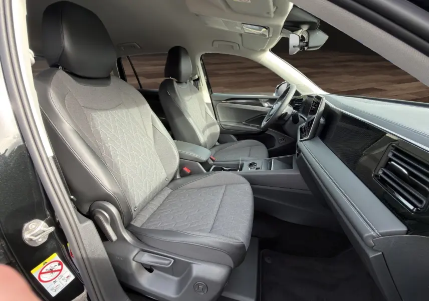 Vue intérieure côté conducteur du Volkswagen Tiguan noir 2026, sièges tissu gris avec accoudoirs et tableau de bord moderne.
