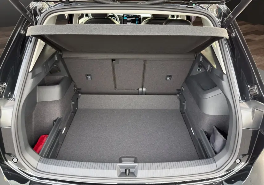 Coffre ouvert vu de l'arrière d'un Volkswagen Tiguan noir 2026, montrant un espace de chargement propre et rangements latéraux.