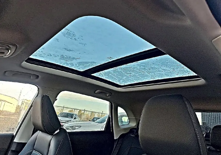 Toit panoramique en verre vu de l'intérieur sur les sièges avant en similicuir noir d'un MG Motor ZS blanc.