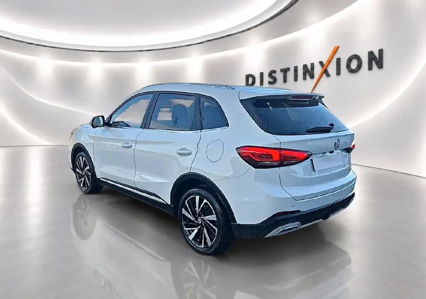 Vue 3/4 arrière droite d'un MG Motor ZS blanc 2026 avec jantes alliage et feux arrière LED dans un showroom lumineux.
