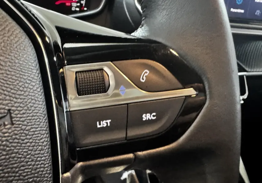 Gros plan sur les commandes gauche du volant cuir de la Peugeot 208 PureTech 75 S&S Active 2024, intérieur noir.