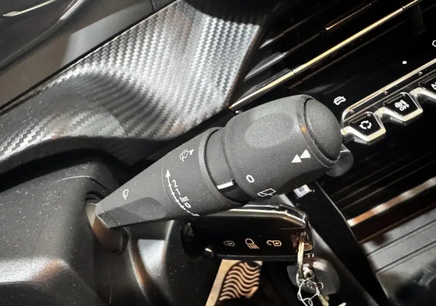 Gros plan sur la commande d’essuie-glace noire et la clé insérée dans le contacteur d’une Peugeot 208 blanche, intérieur noir.