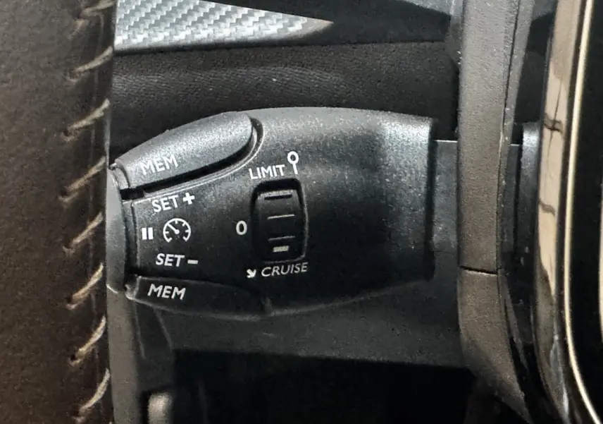 Gros plan sur la commande de régulateur de vitesse noire à gauche du volant dans l’habitacle d’une Peugeot 208 blanche 2024.