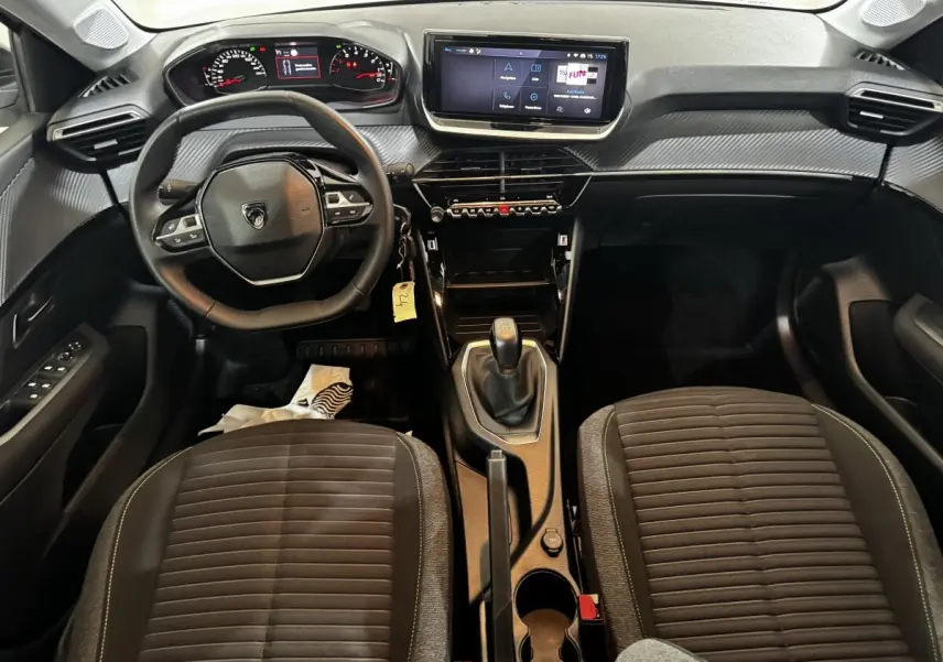 Vue intérieure avant du Peugeot 208 PureTech 75 S&S Active 2024, tableau de bord noir avec écran tactile central et volant cuir multifonctions.