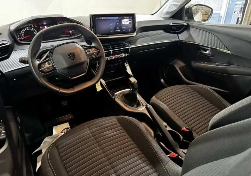 Vue intérieure avant droite du tableau de bord et des sièges noirs de la Peugeot 208 PureTech 75 S&S Active 2024.
