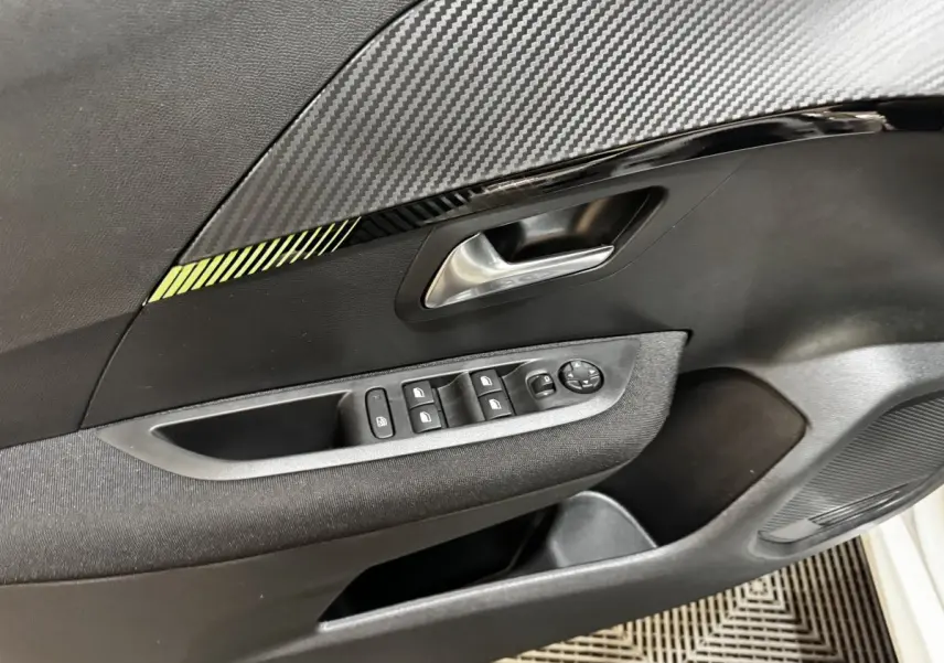 Détail de la porte intérieure côté gauche de la Peugeot 208 PureTech 75 S&S Active avec commandes de vitres et décor carbone.