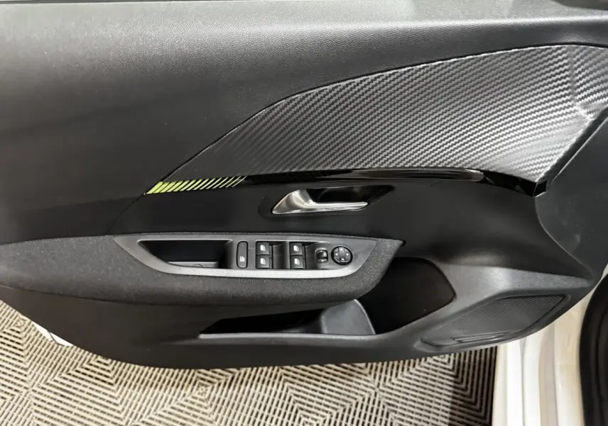 Vue rapprochée de la porte avant gauche noire avec insert effet carbone et commandes électriques sur Peugeot 208 blanc 2024.