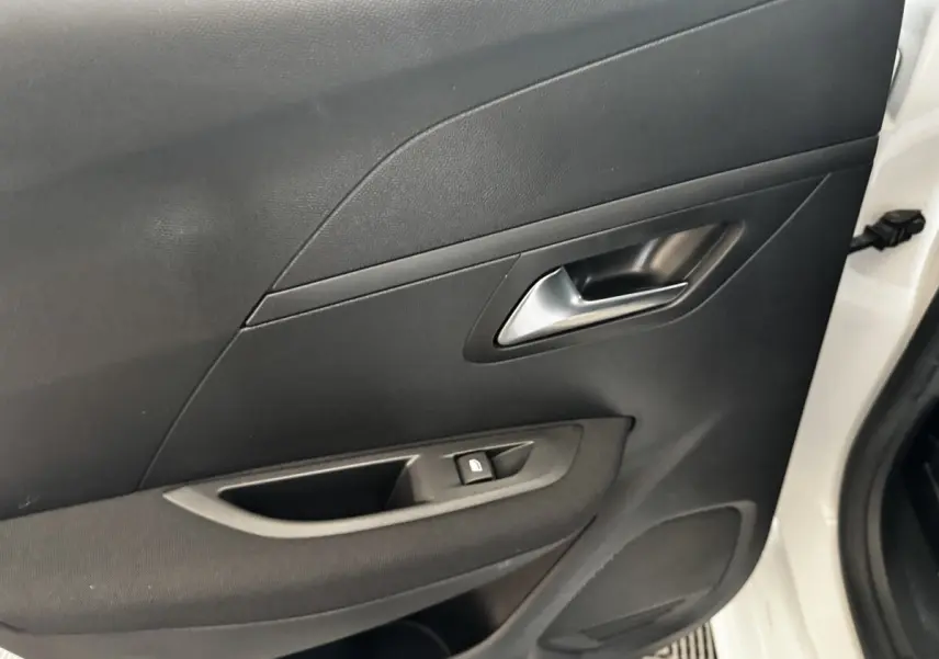 Vue rapprochée de la porte avant droite noire d’une Peugeot 208 blanche, avec poignée et commande de vitre.