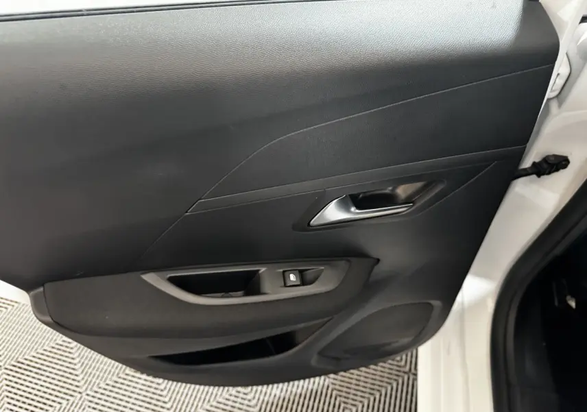 Vue rapprochée de la porte arrière droite noire d'une Peugeot 208 blanche, avec poignée et commande de vitre.