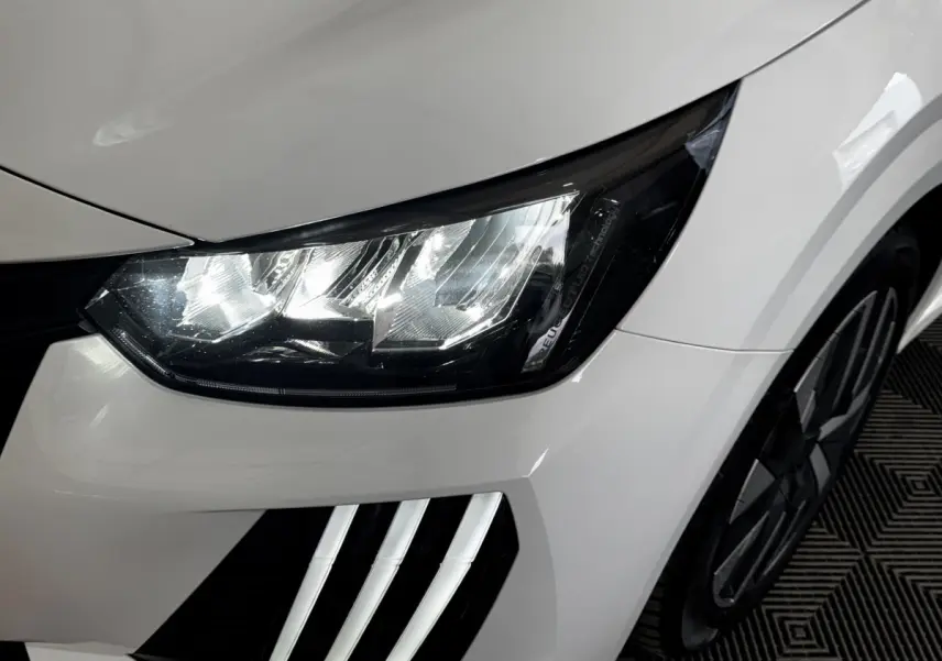 Gros plan sur le phare avant gauche et la calandre blanche d'une Peugeot 208 PureTech 75 S&S Active 2024.