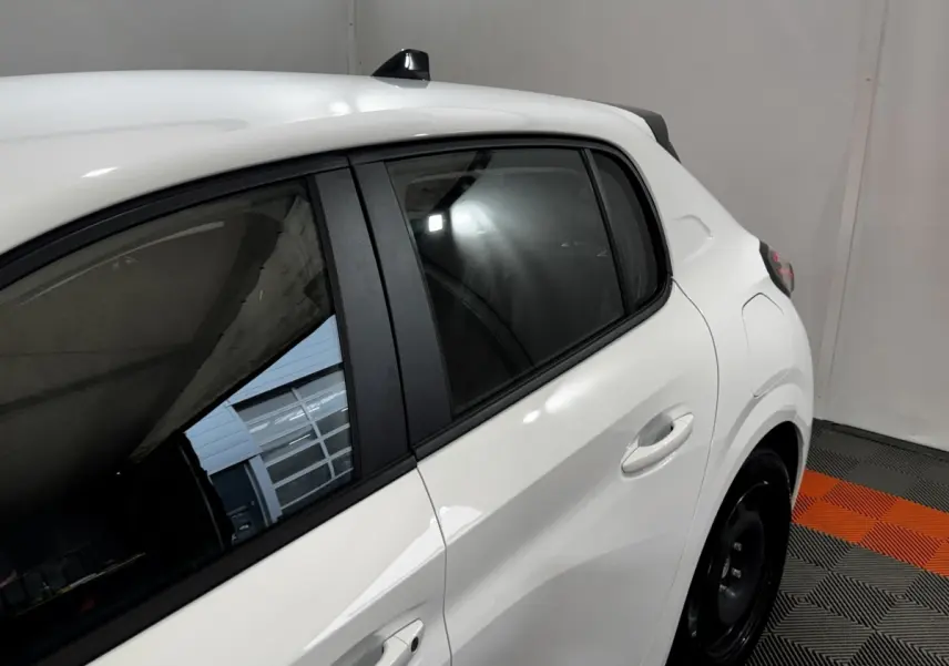 Vue latérale droite rapprochée d’une Peugeot 208 blanche, mettant en valeur la porte arrière et la vitre teintée.