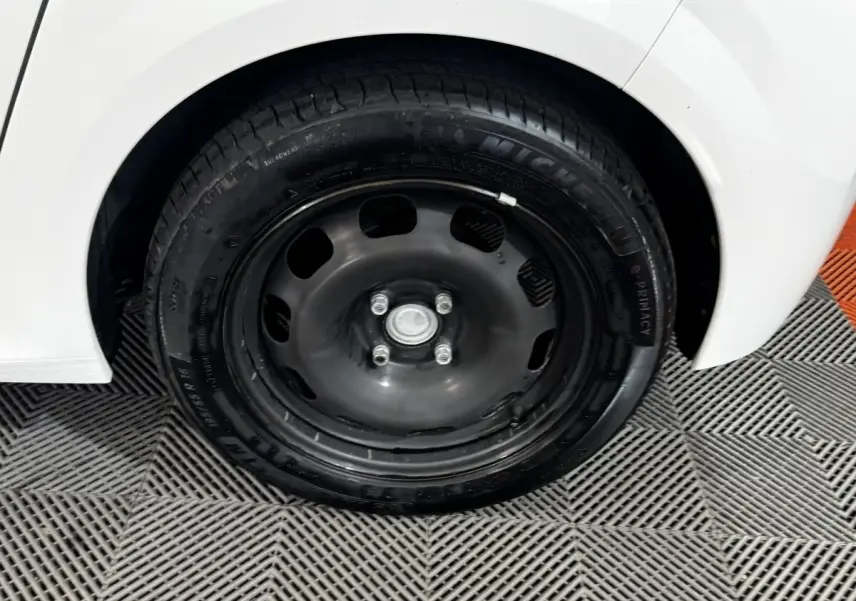 Gros plan sur la roue arrière droite noire de la Peugeot 208 blanche PureTech 75 S&S Active 2024.