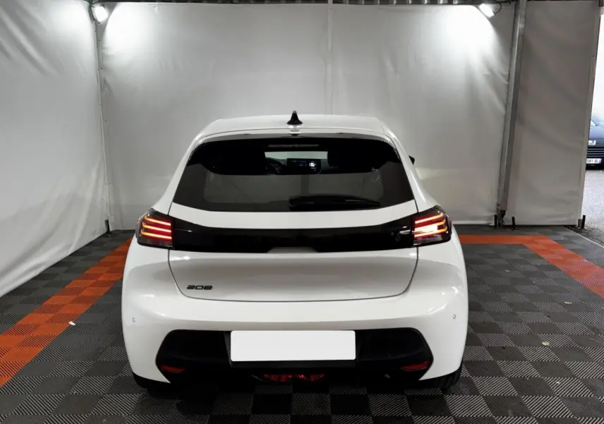 Vue arrière d'une Peugeot 208 blanche 2024 avec feux arrière LED allumés dans un espace fermé.