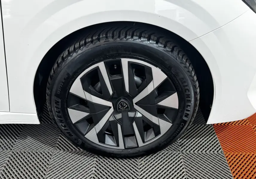 Gros plan sur la roue arrière droite d'une Peugeot 208 blanche avec jante au design géométrique bicolore.