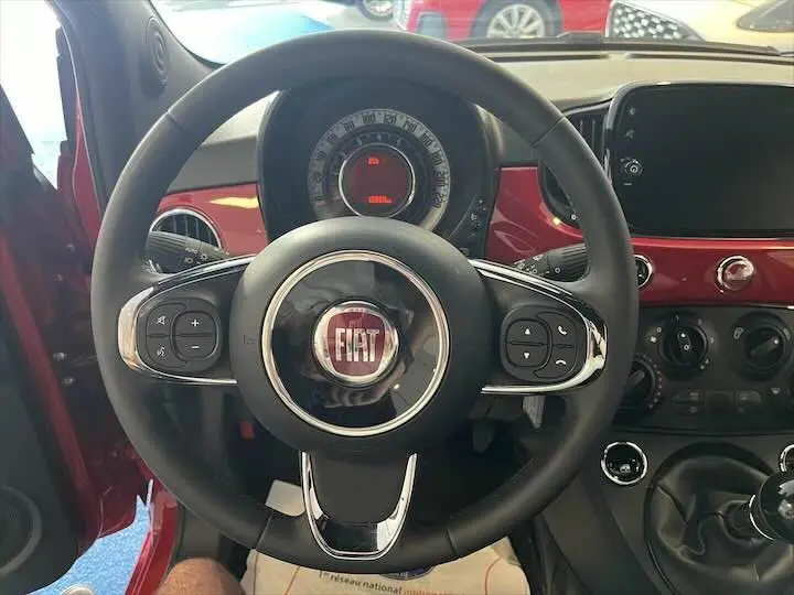 Vue centrée sur le volant noir de la Fiat 500 rouge 2023, avec tableau de bord et commandes visibles en arrière-plan.