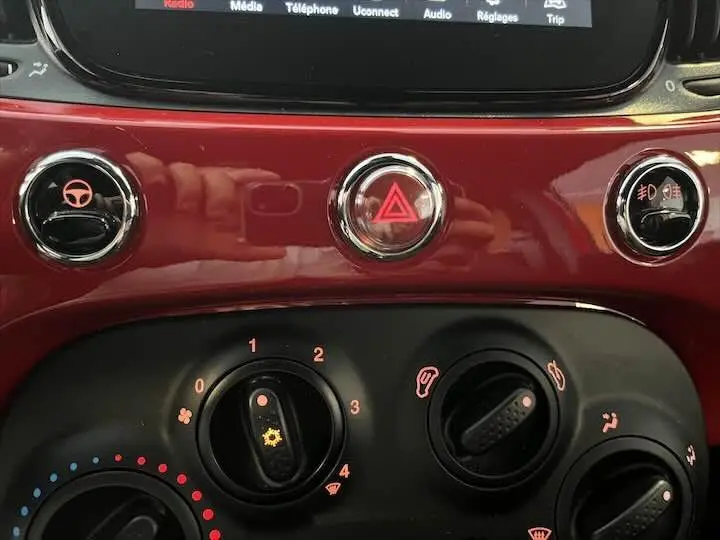 Gros plan sur la console centrale rouge brillante de la Fiat 500 2023 avec commandes climatisation et bouton de warning au centre