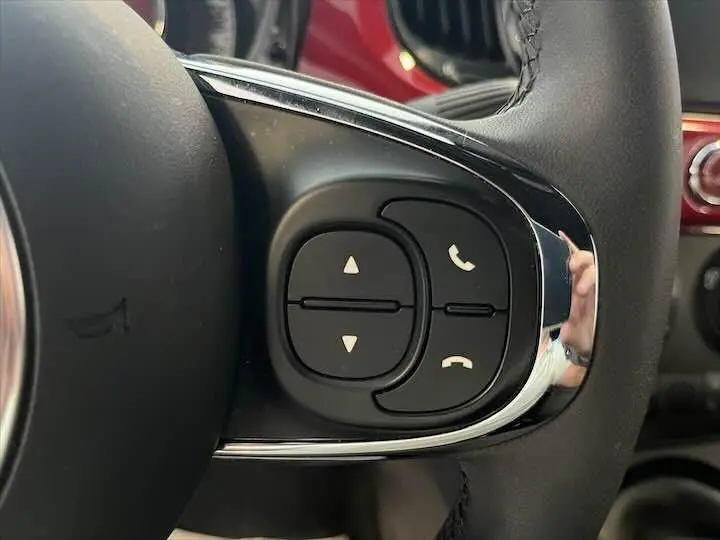 Gros plan sur les commandes du volant côté droit d'une Fiat 500 rouge 2023, boutons de téléphone et navigation.