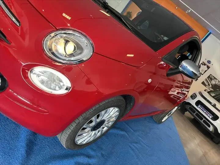 Vue 3/4 avant gauche d'une FIAT 500 rouge brillante avec rétroviseur chromé en intérieur showroom.