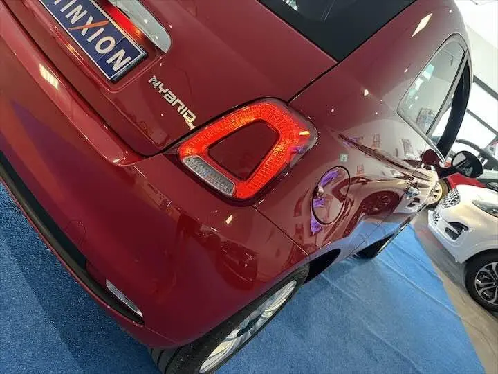 Vue 3/4 arrière droite d'une FIAT 500 rouge 2023 avec feu arrière allumé dans un showroom lumineux.