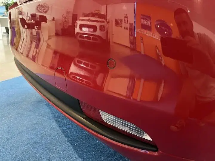 Gros plan sur le pare-chocs arrière rouge d'une Fiat 500 hybride, avec capteurs de recul visibles et reflet intérieur showroom.
