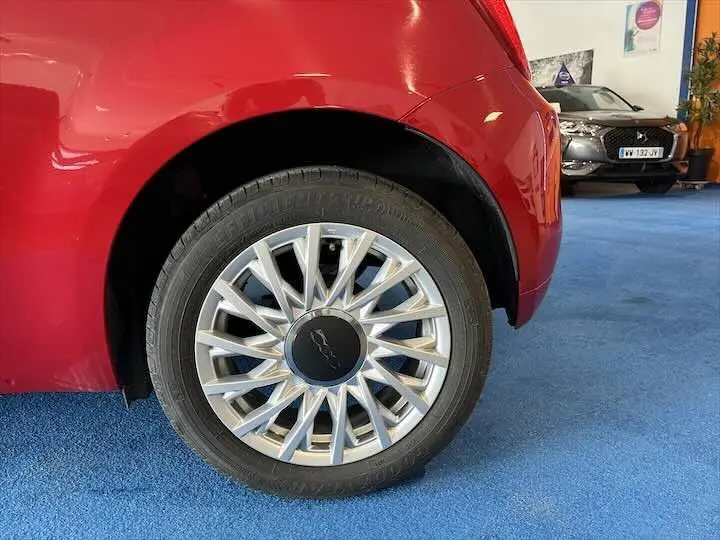 Gros plan sur la roue arrière gauche d'une FIAT 500 rouge 2023 avec jante argentée au design étoilé.