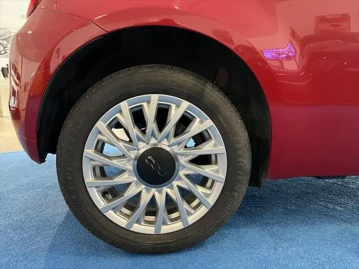 Gros plan sur la roue avant gauche d'une FIAT 500 rouge 2023 avec jante argentée au design étoilé.