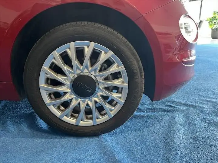 Gros plan sur la roue avant gauche d'une FIAT 500 rouge 2023, mettant en valeur la jante argentée au design étoilé.