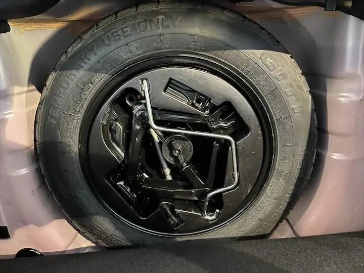 Gros plan sur la roue de secours et le cric noir dans le coffre d'une FIAT 500 rouge 2023.