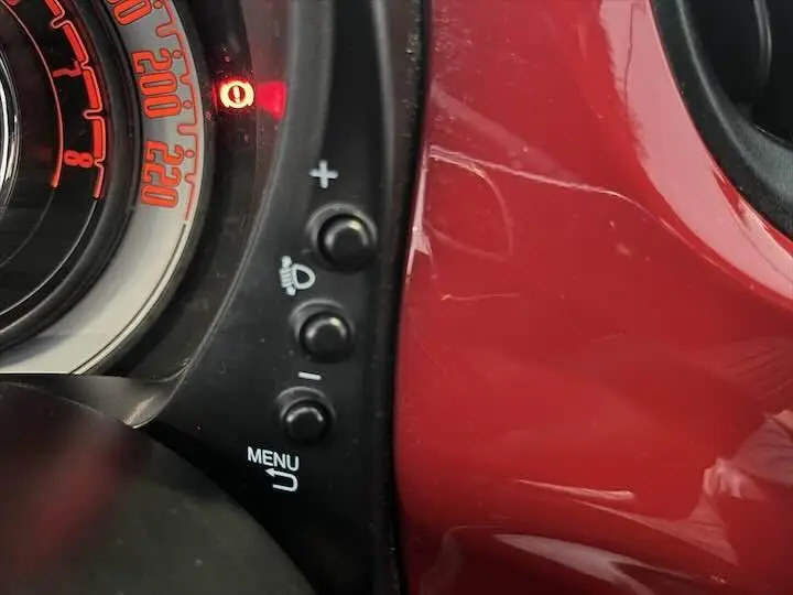 Détail du tableau de bord de la FIAT 500 rouge 2023, montrant les commandes de réglage et le compteur partiel.