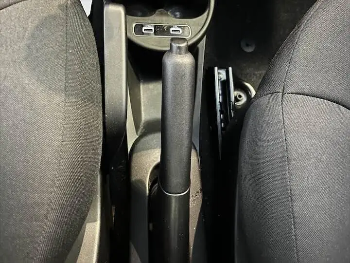 Vue rapprochée de la poignée de frein à main entre les sièges avant noirs d'une Fiat 500 rouge de 2023.