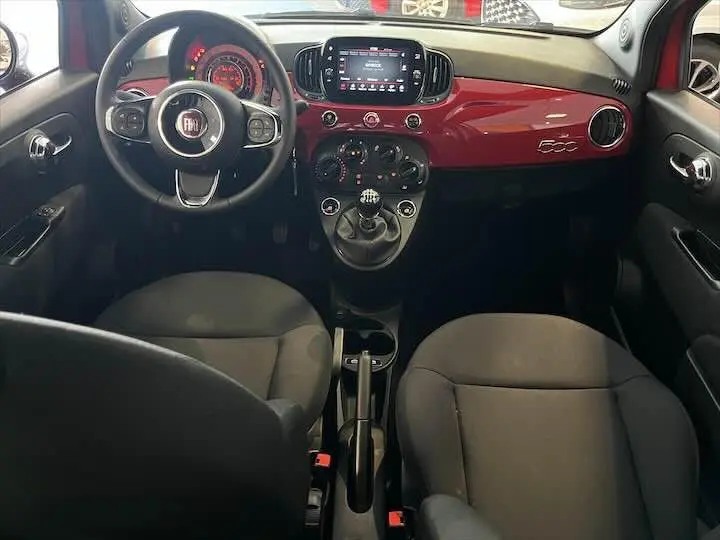 Intérieur avant de la FIAT 500 2023 avec tableau de bord rouge brillant et volant noir, vue centrée sur la console manuelle.